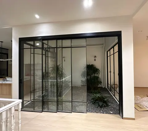 Wide synchronized sliding door with black lattice panels in front of an indoor garden