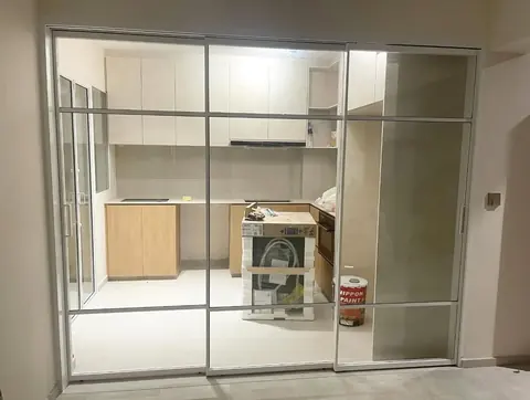 White-framed synchronized sliding door with horizontal lattice bars, closed in front of a kitchen being fitted out